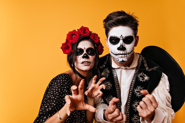 Furious guy and girl with Halloween makeup posing for close-up portrait in orange wall.