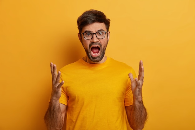 Furious man shouts and gestures with anger, keeps mouth opened