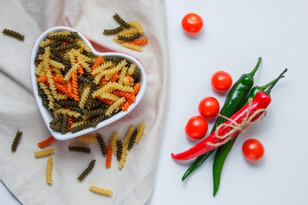 Free Photo fusilli pasta in a bowl with peppers, tomatoes flat lay on white and tablecloth table