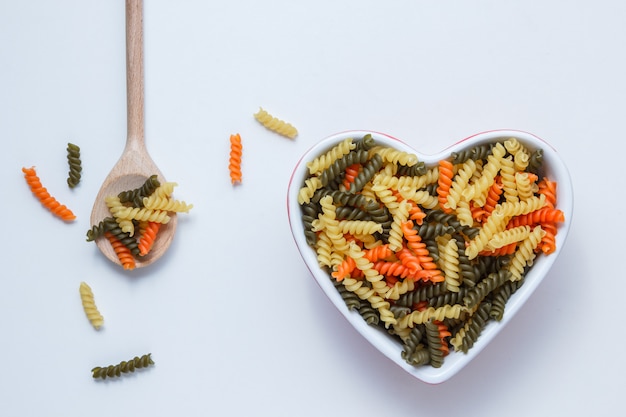 Free Photo fusilli pasta in bowl and wooden spoon on white table, top view.