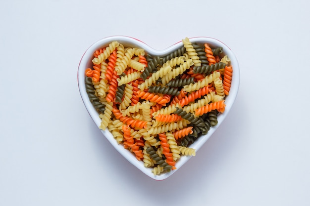 Free Photo fusilli pasta in a heart shaped bowl on white table, top view.