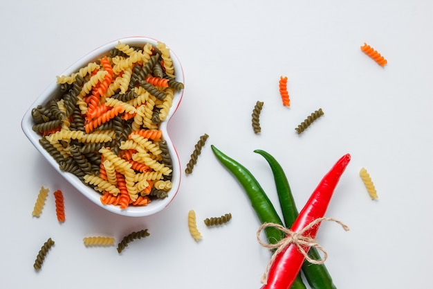 Fusilli pasta with hot peppers in a bowl on white table, top view.