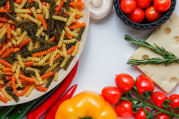 Free Photo fusilli pasta with tomatoes, peppers, mushroom, plant on cheese in a plate on white table, high angle view.