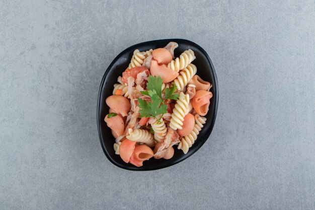 Fusilli and red seashell pasta in black bowl.