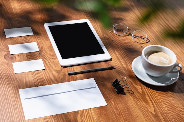 Free photo gadgets, coffee, work tools on a wooden table indoors. creative, cozy workplace at home office, inspirational mock up with plant shadows on surface. concept of remote office, freelance, atmosphere.