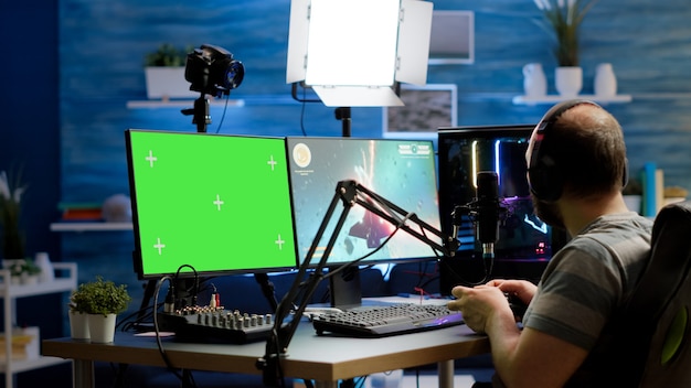 Free photo gamer streaming online videogames on professional powerful computer with green screen, mock up, chroma key display. streamer playing space shooter game at isolated desktop holding wireles controller