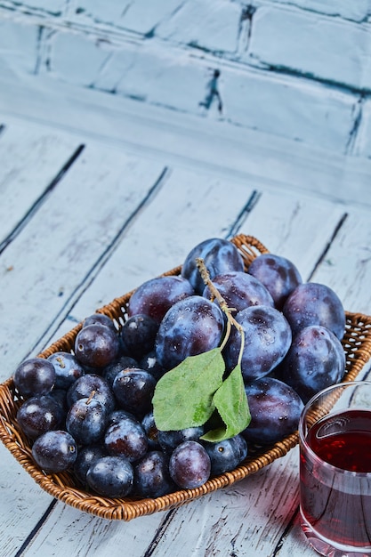 Free Photo garden plums in a basket on a blue background with a glass of juice. high quality photo