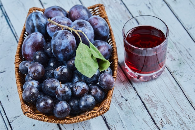 Free Photo garden plums in a basket on blue with a glass of juice.