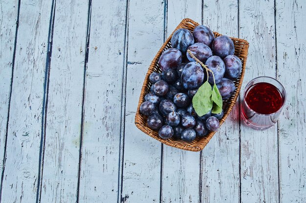 Garden plums on basket on blue with a glass of juice.