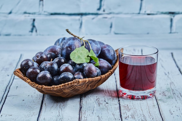 Garden plums on basket on blue with a glass of juice.