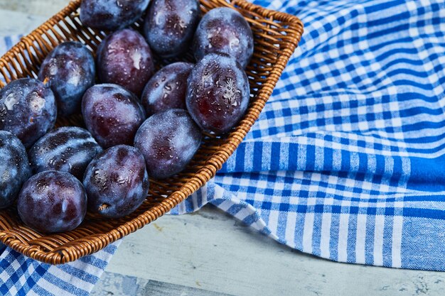 Garden plums on basket on stone table with tablecloth.