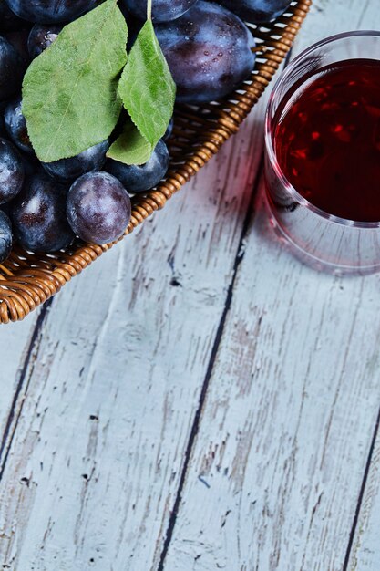 Garden plums in a basket on a wooden table with a glass of juice. High quality photo