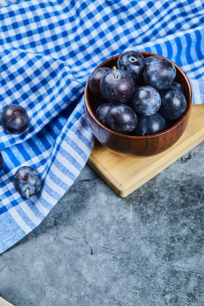 Garden plums in a bowl on marble with tablecloth.