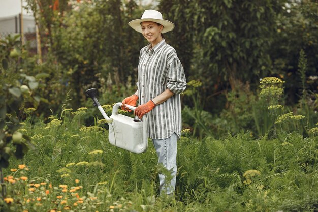 Gardening in summer. Woman watering flowers with a watering can. Girl wearing a hat.