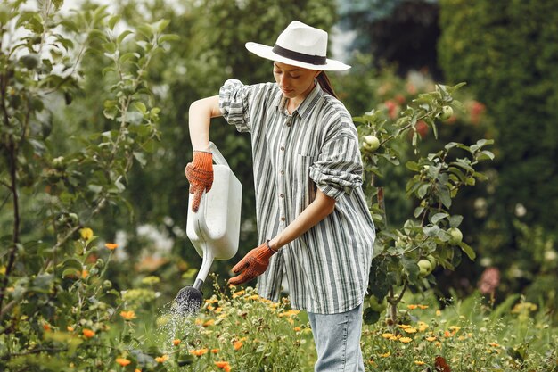 Gardening in summer. Woman watering flowers with a watering can. Girl wearing a hat.