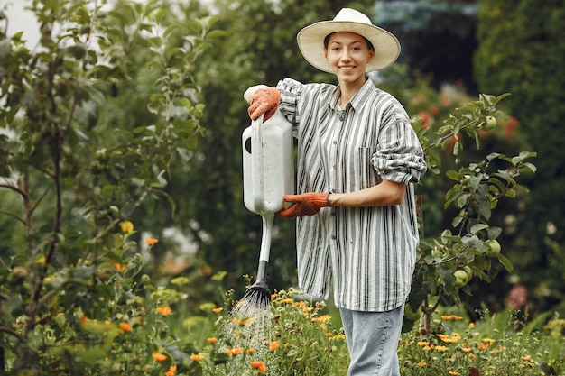 Gardening in summer. Woman watering flowers with a watering can. Girl wearing a hat.