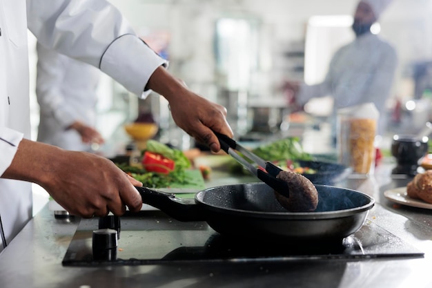 Free photo gastronomy expert cooking succulent beef patty in hot pan while cooking gourmet dish for dinner service at restaurant. food industry worker preparing meat for meal in professional kitchen.