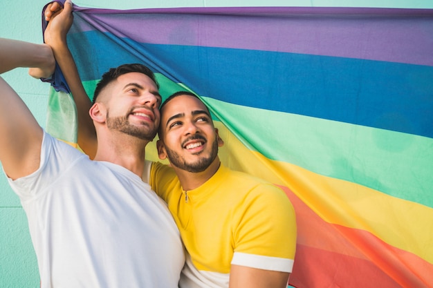 Gay couple embracing and showing their love with rainbow flag.