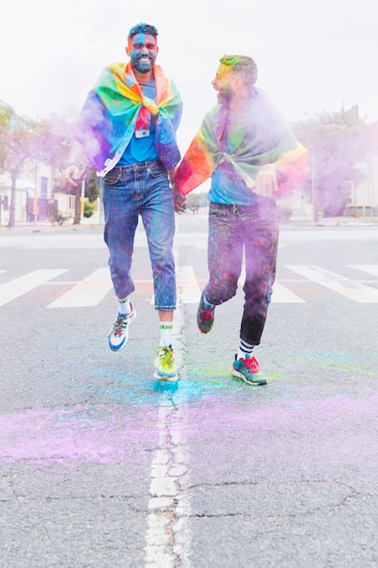 Free photo gay couple in multicolored holi powder running down road