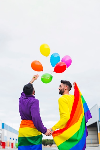 Free photo gay couple releasing rainbow balloons in sky