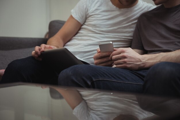 Gay couple sitting on sofa and looking at digital tablet