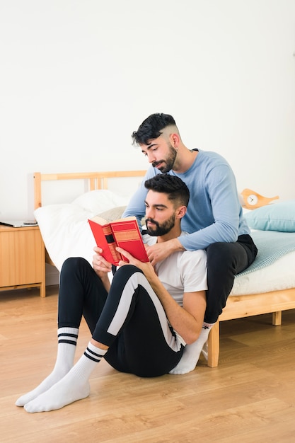 Gay couple sitting with his boyfriend reading the book in the bedroom