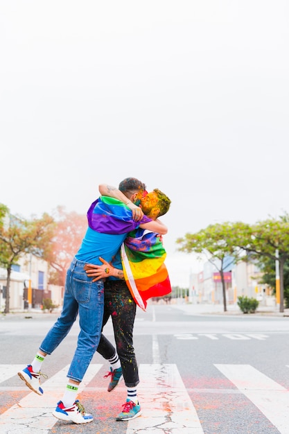 Gays with rainbow flags hugging on pedestrian crossing 