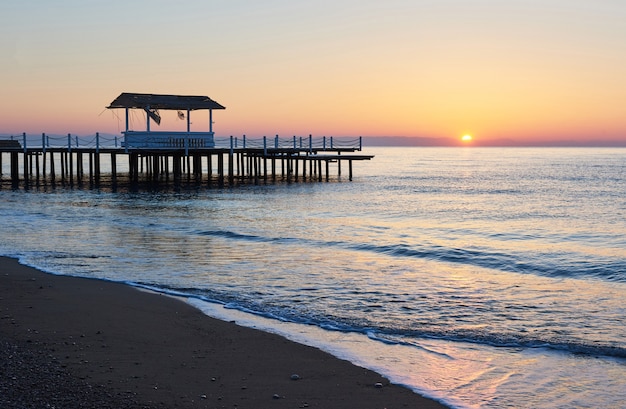 Gazebo on the wooden pier into the sea with the sun at sunset.