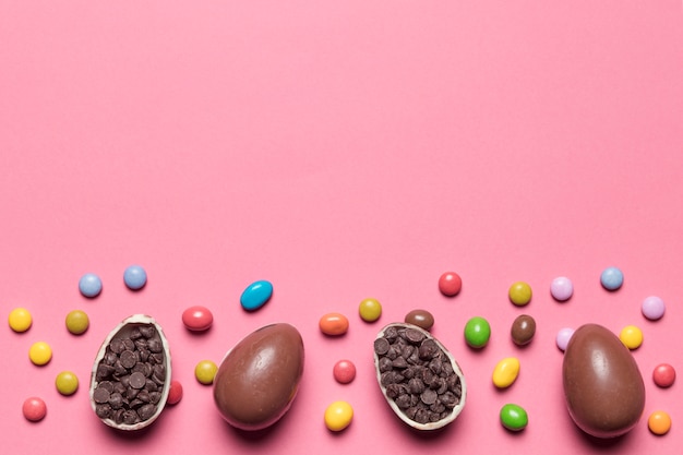 Gem candies; chocolate easter eggs filled with choco chips on pink background