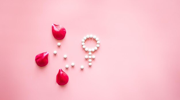 Gender venus symbol made of pills and peony flower petals on a pink background