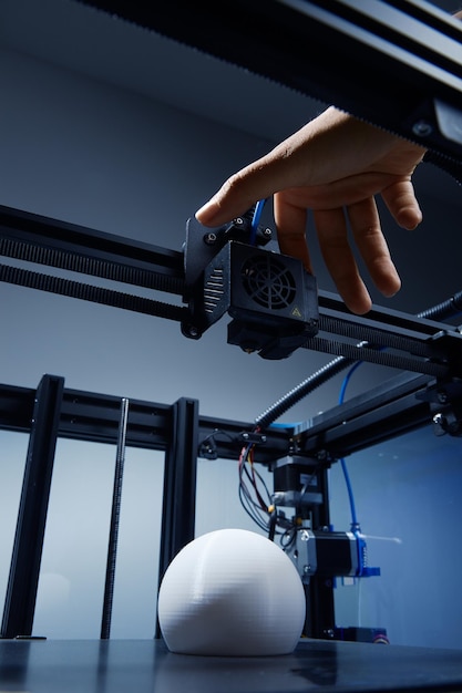 A genderneutral hand modifying settings in 3d printer to finish printing round white object from recycled plastic Futuristic concept of new working possibilities for small businesses by 3D printing