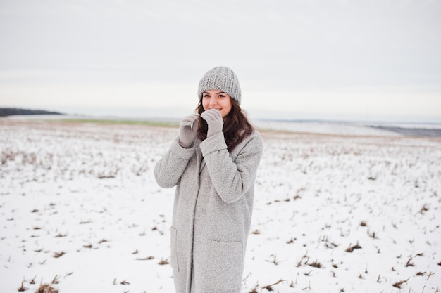 Gentle girl in gray coat and hat against snow landscape