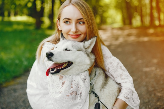  gentle girl with light hair dressed in white dress is playing along with her dog