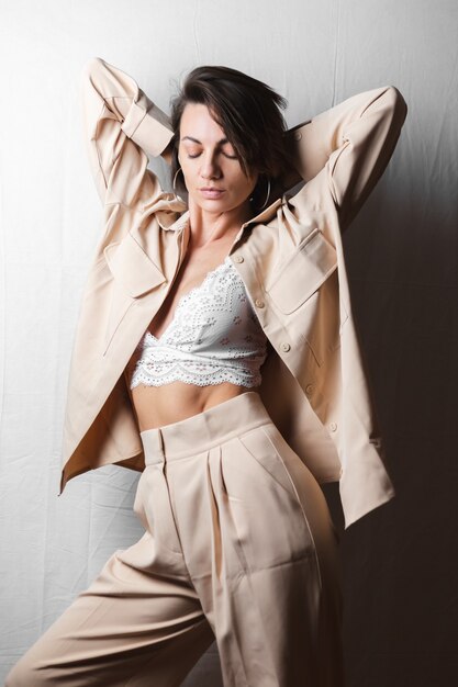 Gentle portrait of a beautiful young woman with big breasts in a beige suit and white lace bra on a gray white