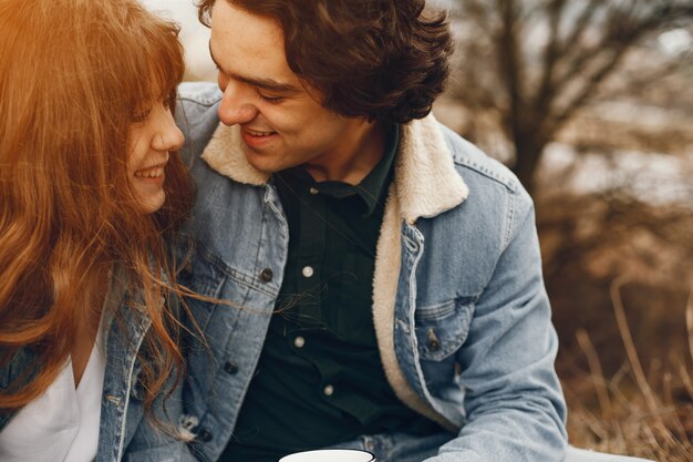 gentle and stylish couple sitting in the autumn park and drinking a tea