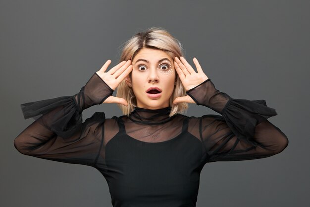 Free photo genuine human emotions and feelings. emotional beautiful blonde girl in trendy clothes and accessories expressing true astonished reaction on unexpected news, opening mouth in full disbelief