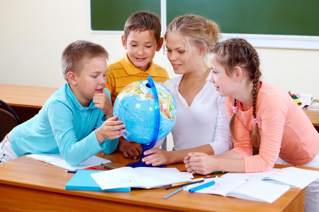 Geography teacher and students looking at globe