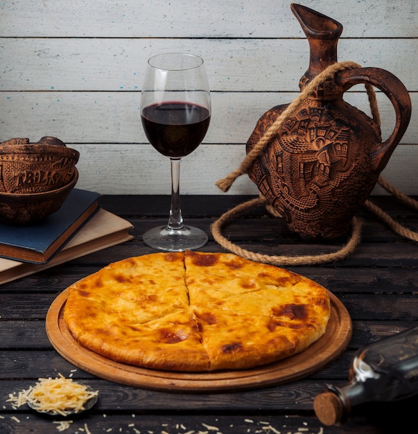 Free photo georgian khachapuri served on wood pizza board with red wine