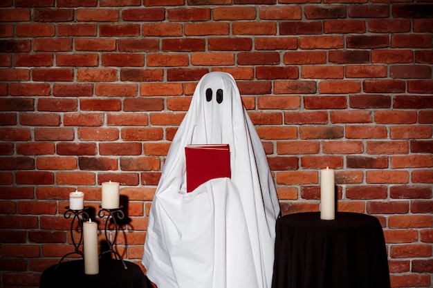 Free photo ghost holding book over brick wall. halloween party.