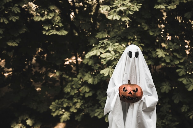 Free photo ghost holding pumpkin and standing in forest