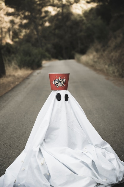 Ghost with popcorn box on head sitting on countryside road