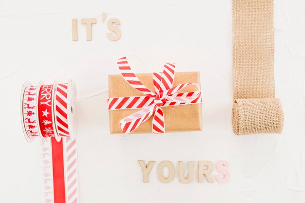 Gift box in craft paper with ribbon near elastic roller and inscription 