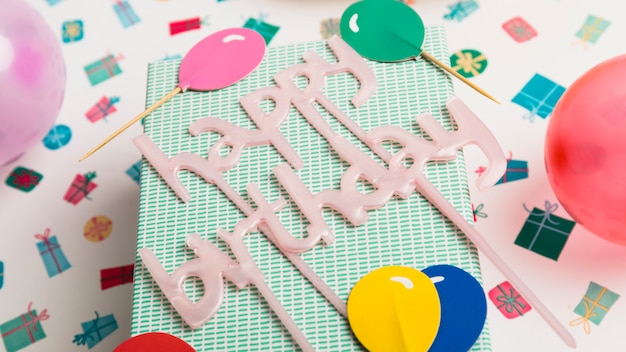 Gift box and happy birthday sign between ornament and bright balloons