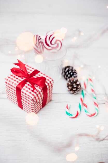 Gift box near glass with lollipops, candy canes and illuminated fairy lights