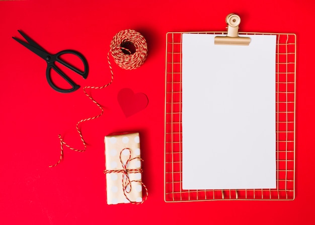 Gift box near ornament heart, clipboard, scissors and threads 