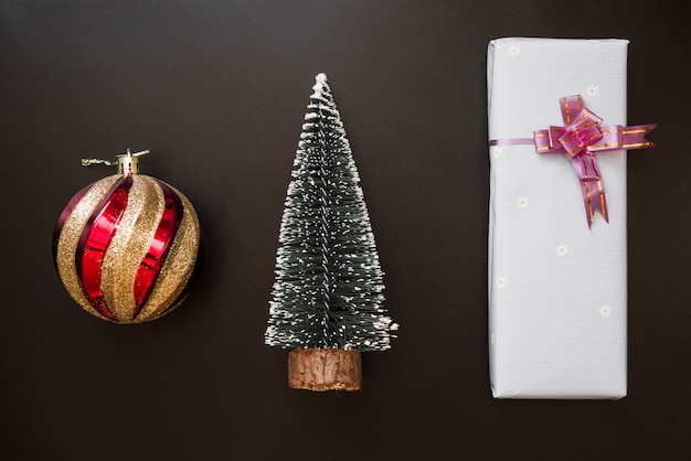 Gift box with bow near decorative ball and fir tree