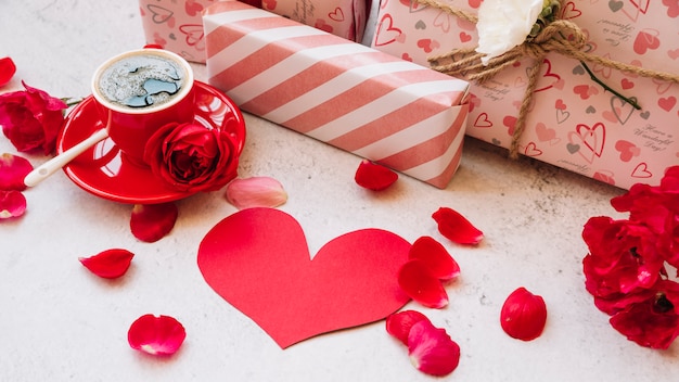 Free photo gift boxes in wrap near flower petals, paper heart and cup with drink