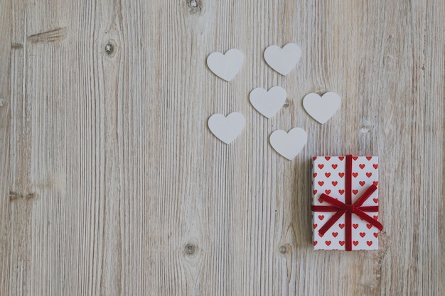 Free photo gift of polka dots with red bow with paper hearts on a wooden table