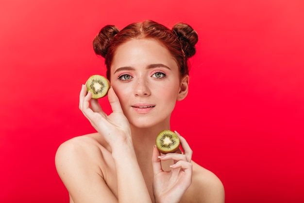 Free photo ginger girl holding kiwi. studio shot of caucasian adorable woman with tropical fruits.