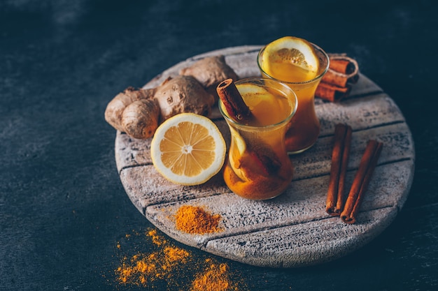 Ginger powder in tea cups with lemon, ginger and dry cinnamon high angle view on wood on a dark textured background